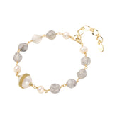 Bracelet with cloudy quartz beads, freshwater pearls, and gold-wrapped baroque pearl centerpiece on white background.