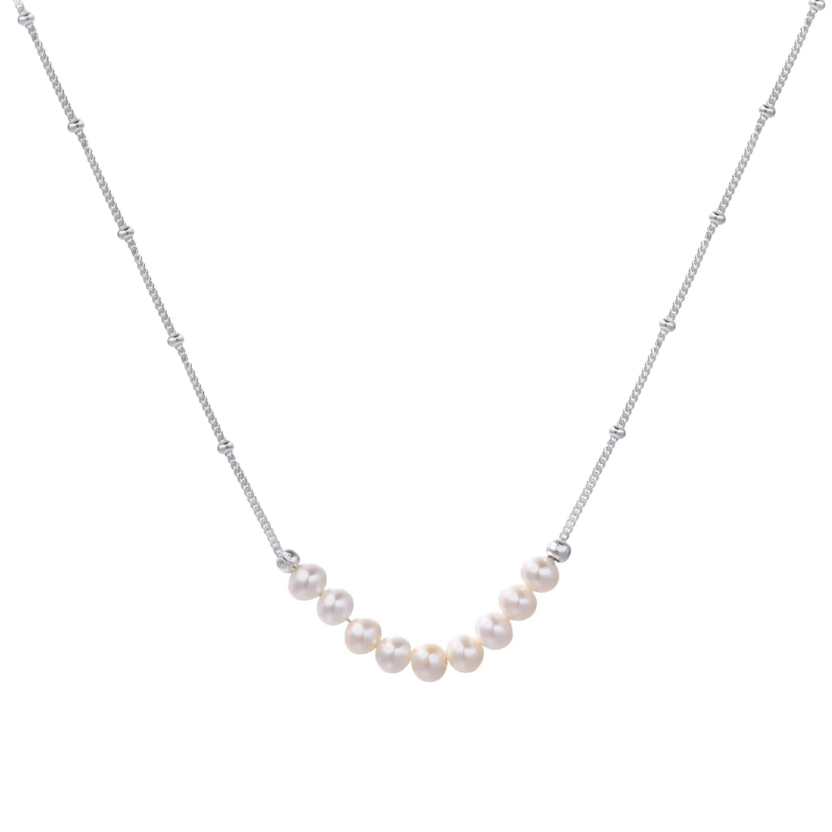 Delicate sterling silver chain necklace with small freshwater pearls arranged in a curved smile arc on cream background.
