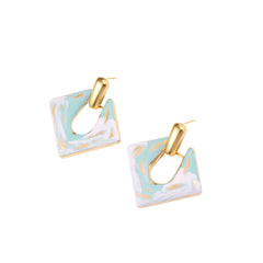 Geometric square enamel earrings with marbled turquoise and lavender pattern, gold U-shaped connector on cream background.